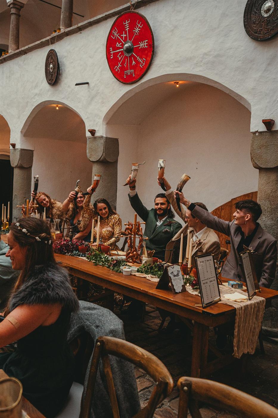 Festgesellschaft in Gewandung hebt Trinkhörner zum Skål an der Tafel im Arkadenhof