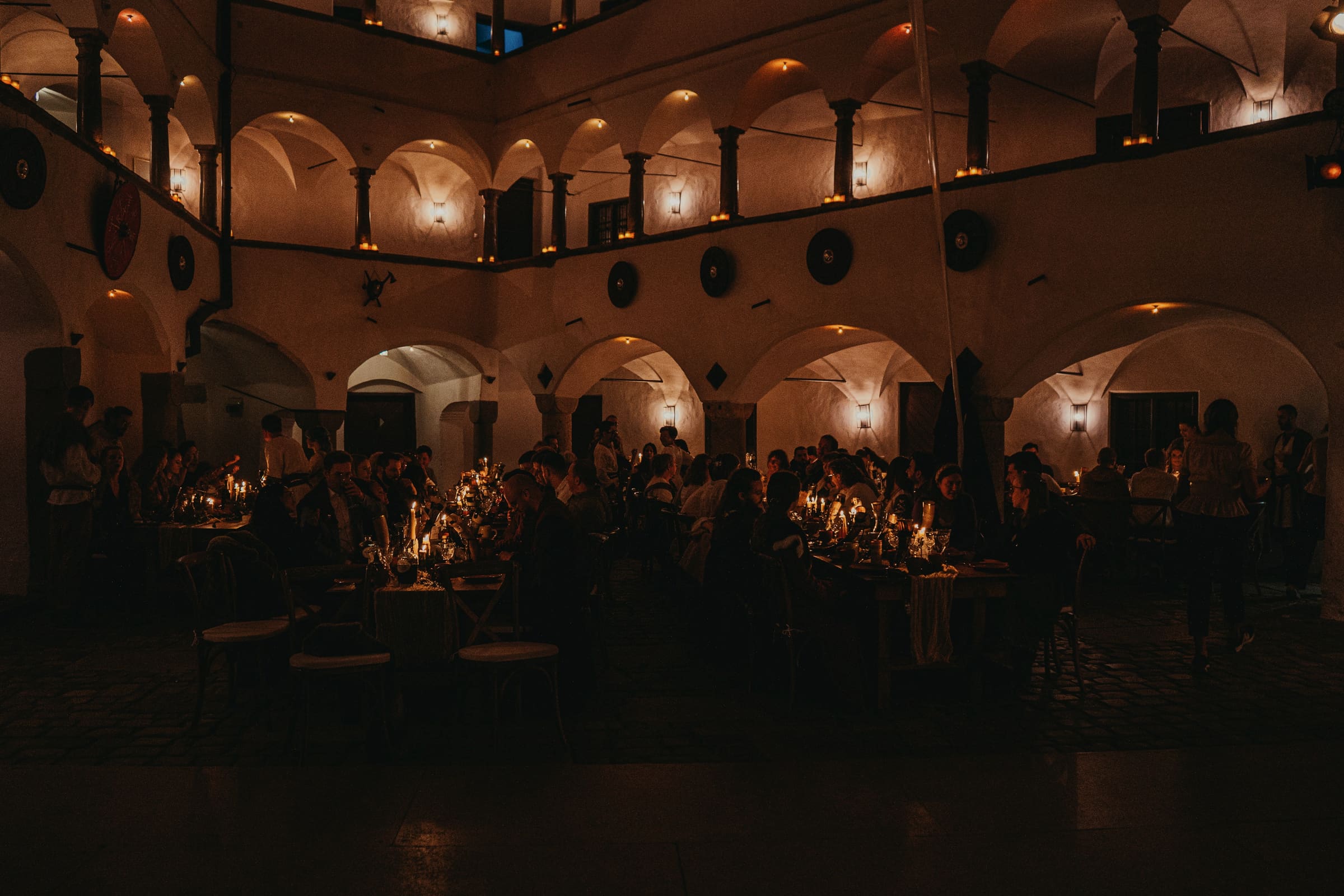 Kerzenbeleuchteter Arkaden-Innenhof einer Burg bei Nacht — Festtafeln und Gäste in Gewandung als Silhouetten